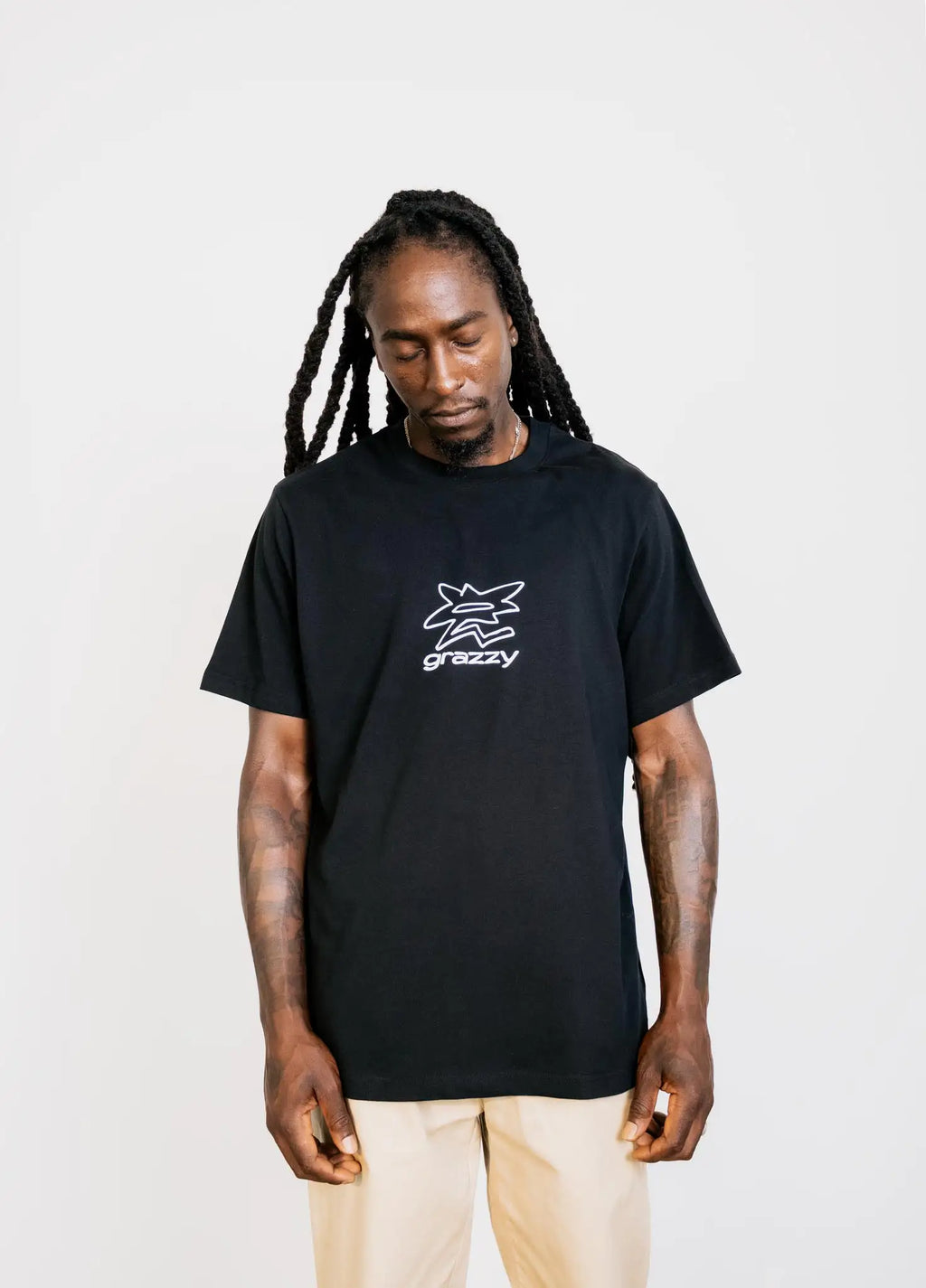 Mid-shot of model in studio wearing the grazzy Symbol t-shirt in the Black colorway, featuring a white flower-like graphic logo mark on the chest.