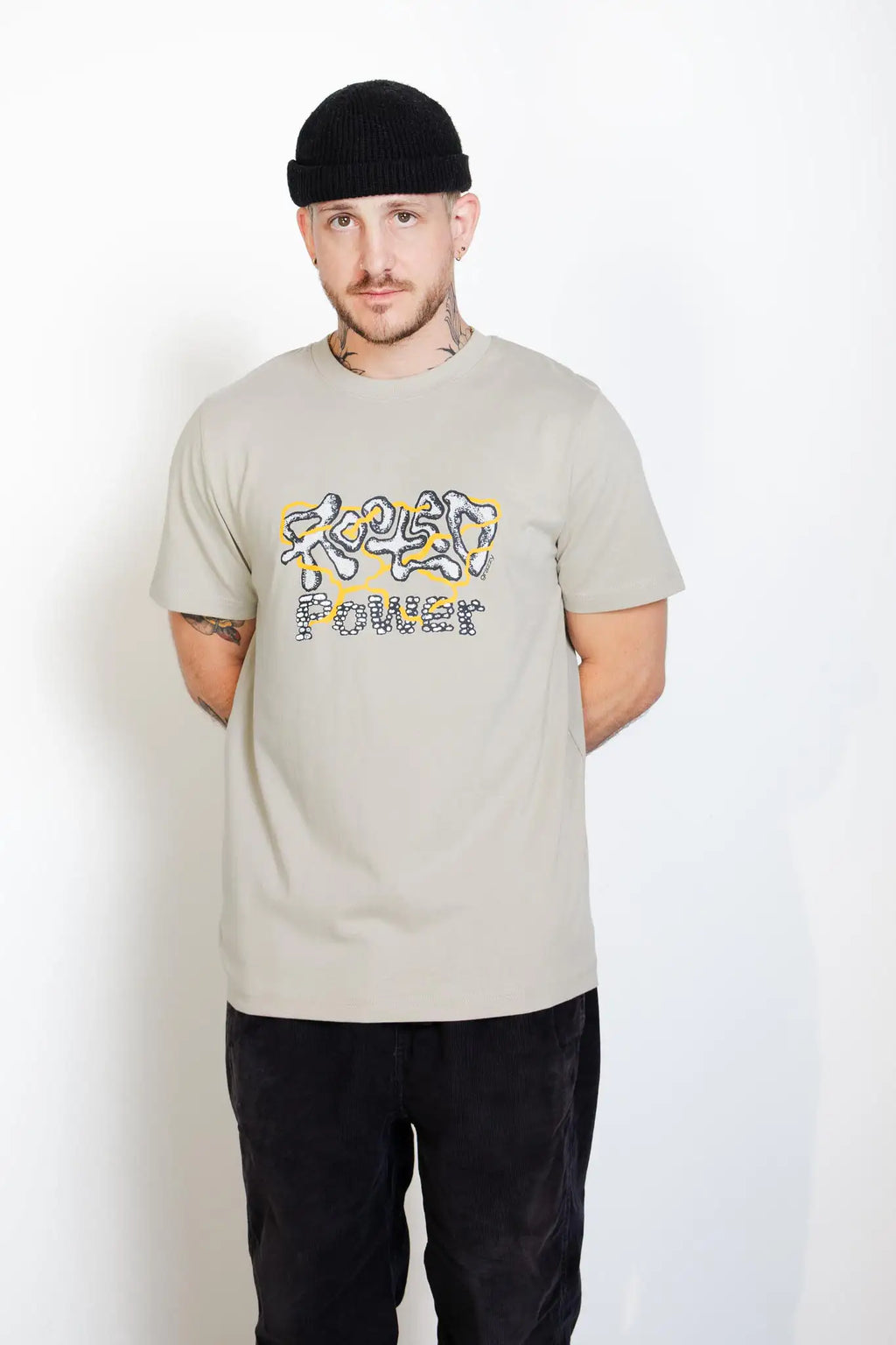 Front view of a model in studio wearing the grazzy Rooted Power graphic t-shirt in the Stone colorway and a black beanie.